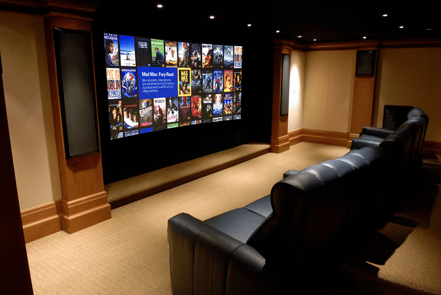 A modern audio/video installation in Atlanta features leather recliner seats facing a large screen displaying a grid of colorful movie posters; the room is softly lit with carpeted floors and wood-paneled walls.